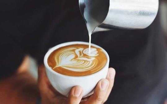 person holding a latte and pouring milk